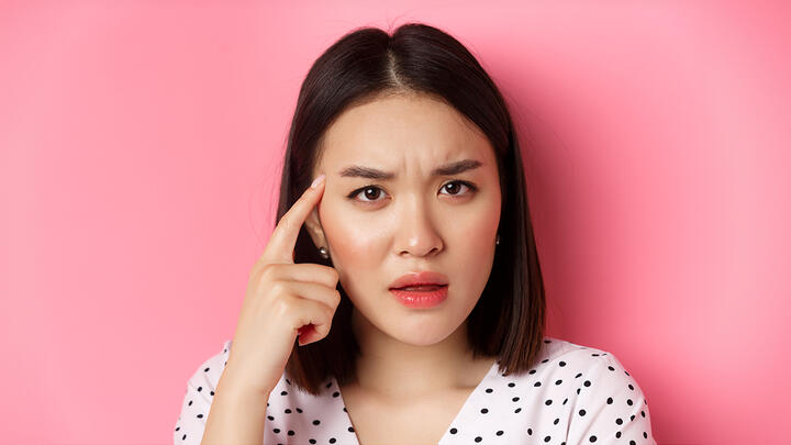 Young woman with dark bob hairstyle frowning, her finger touching her temple